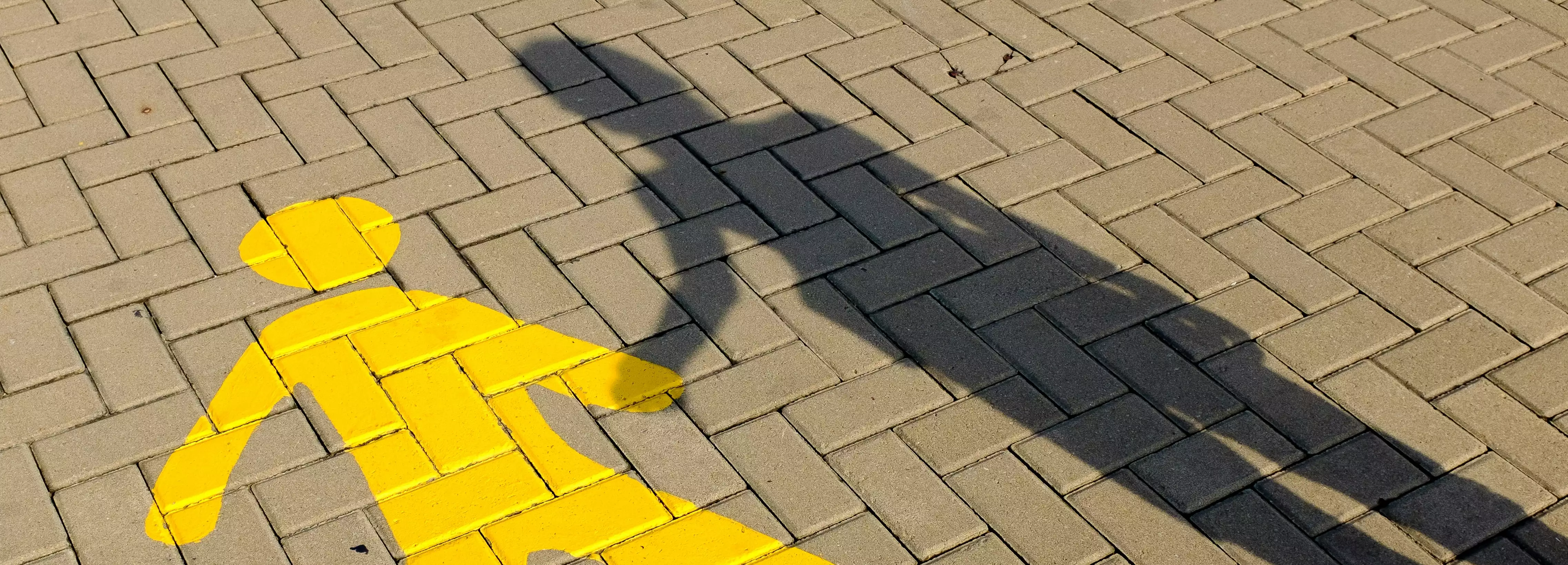 The shadow of a kid holding hands with a figure painted on the pavement in yellow.