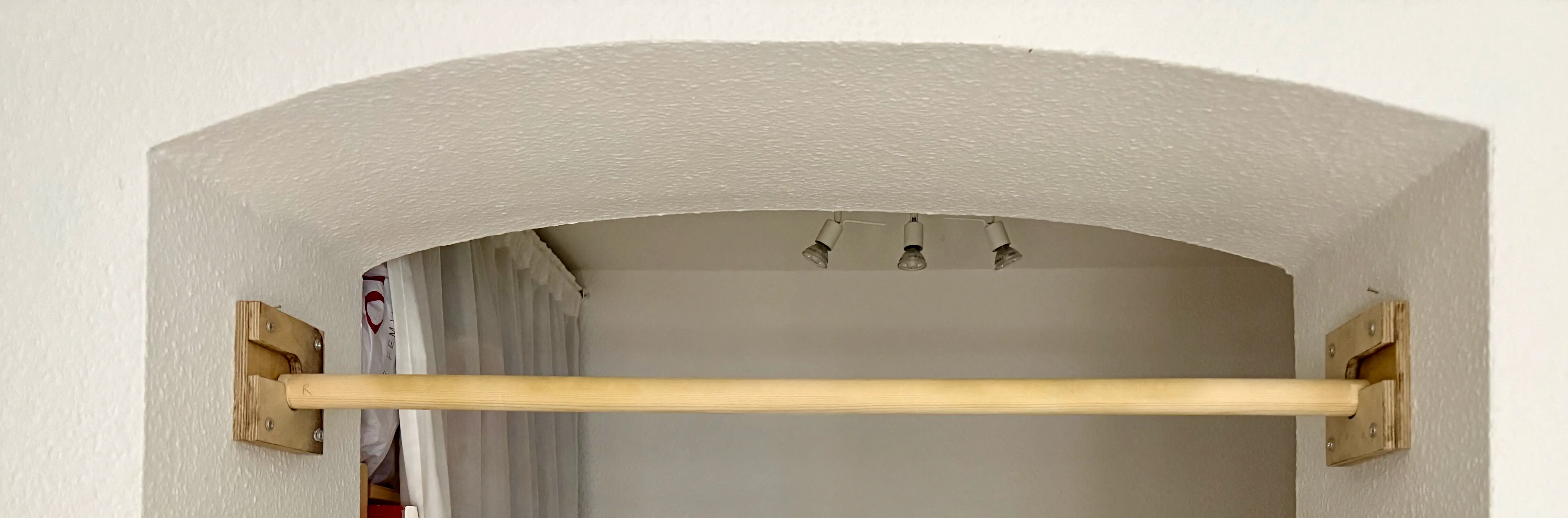 A wooden pullup bar mounted inside a wall opening with a plywood bracket on each side.